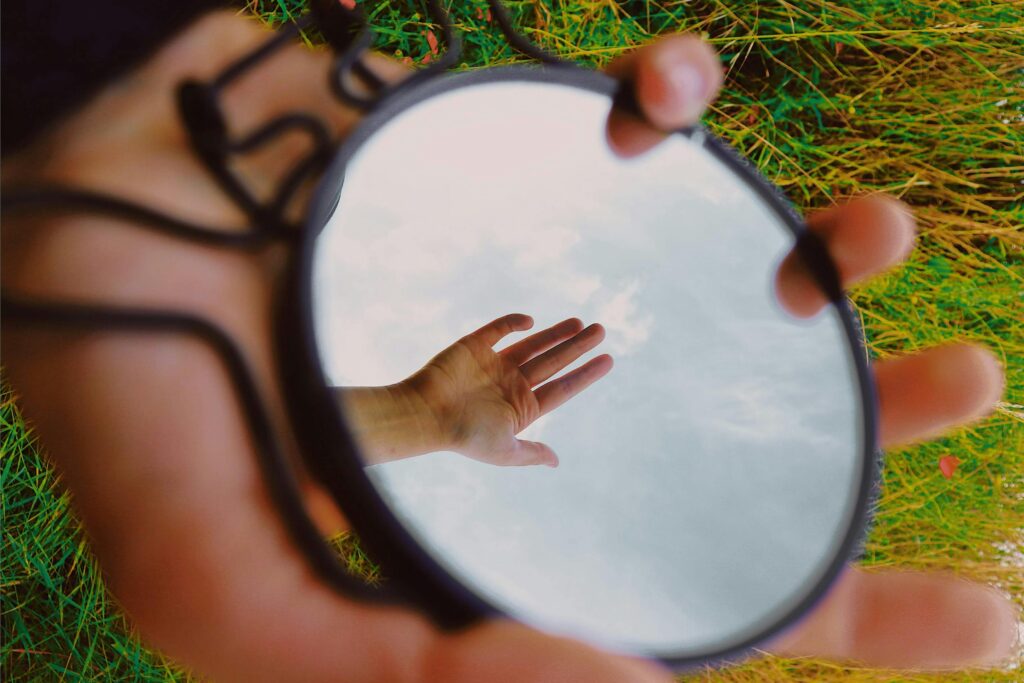 A hand reflecting in a pocket-size mirror held over green grass. Surreal outdoors image.