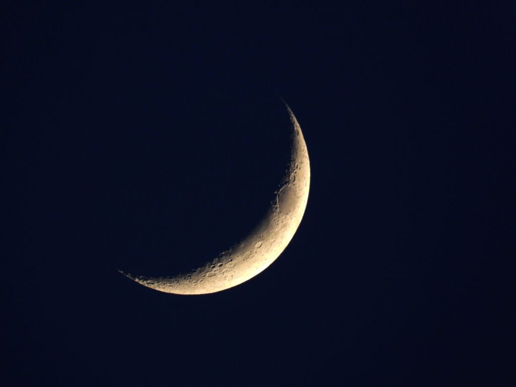 A detailed close-up of the crescent moon set against a clear night sky, showcasing lunar craters.