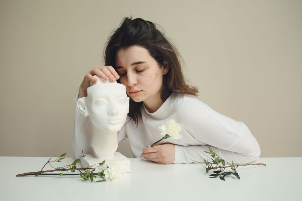 Young woman in white long sleeves lovingly holding a bust sculpture on a table.