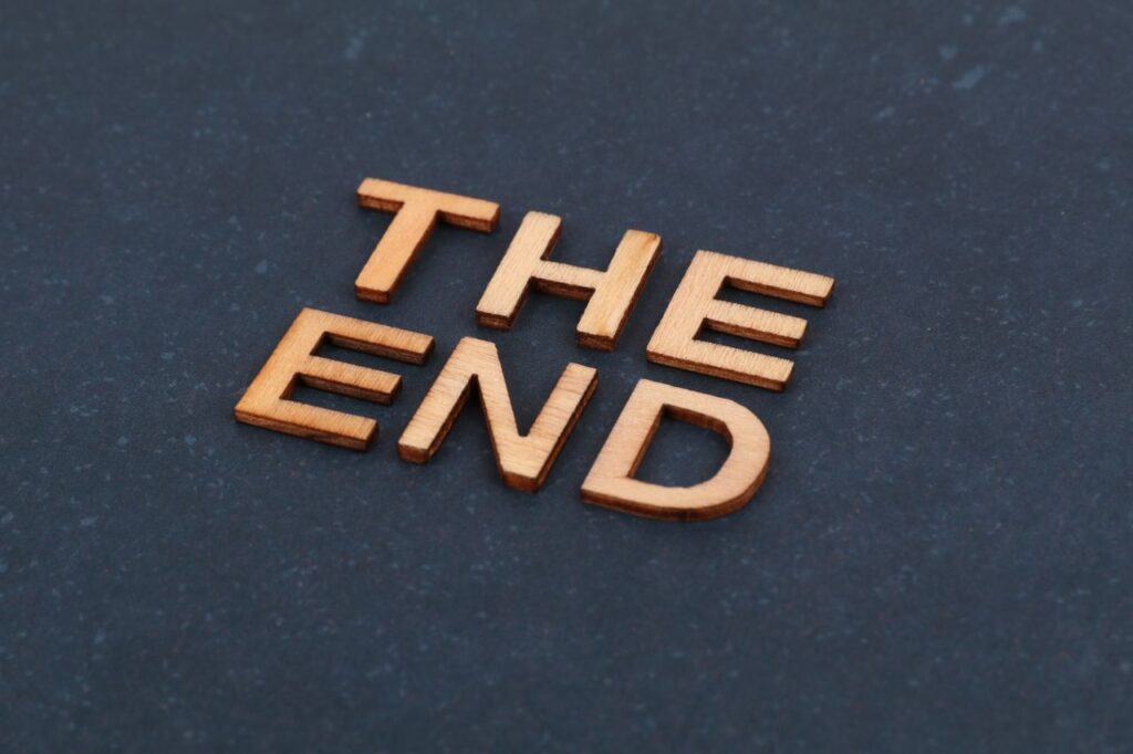 Wooden block letters spelling 'The End' on dark surface, artistic composition.